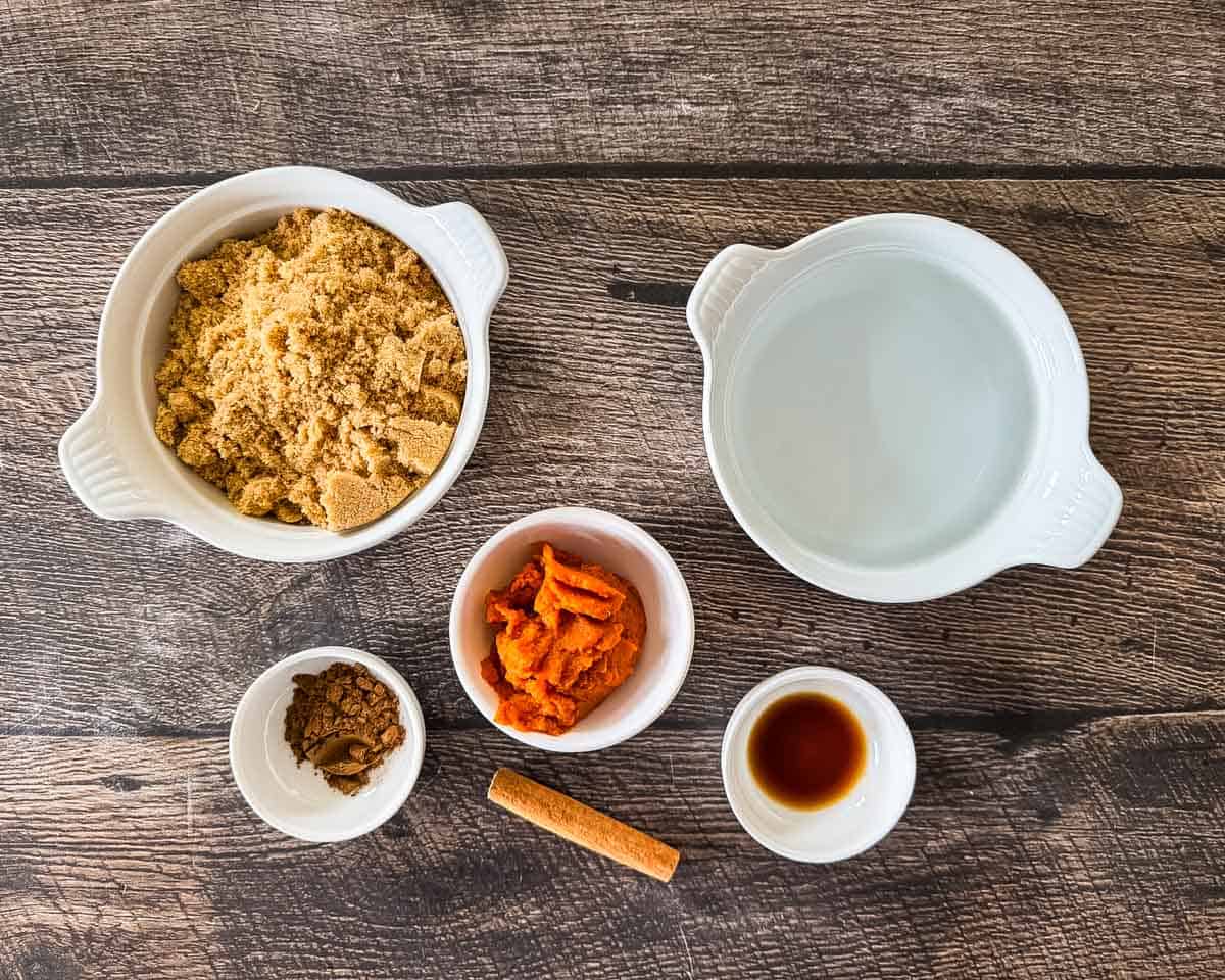 Ingredients for pumpkin spice coffee syrup in white bowls on a wooden counter.