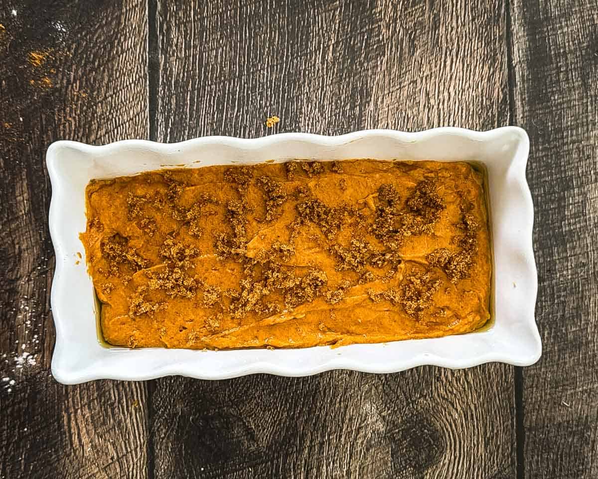 Unbaked sourdough discard pumpkin bread batter sprinkled with demerara sugar in a white loaf pan.
