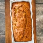 Freshly baked sourdough discard pumpkin bread with a golden brown, cracked crust and demerara sugar topping in a white loaf pan.