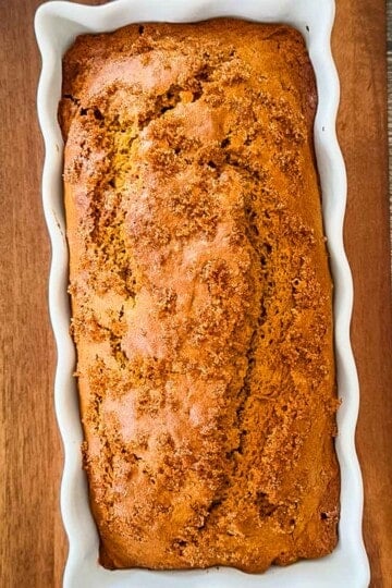 Freshly baked sourdough discard pumpkin bread with a golden brown, cracked crust and demerara sugar topping in a white loaf pan.