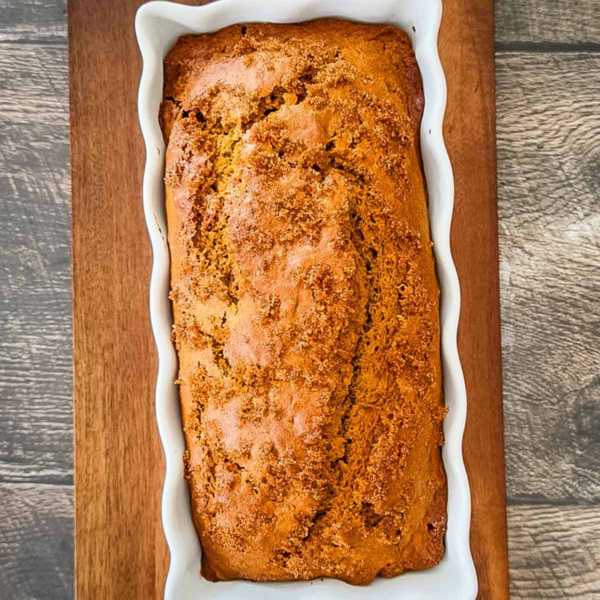 Freshly baked sourdough discard pumpkin bread with a golden brown, cracked crust and demerara sugar topping in a white loaf pan.