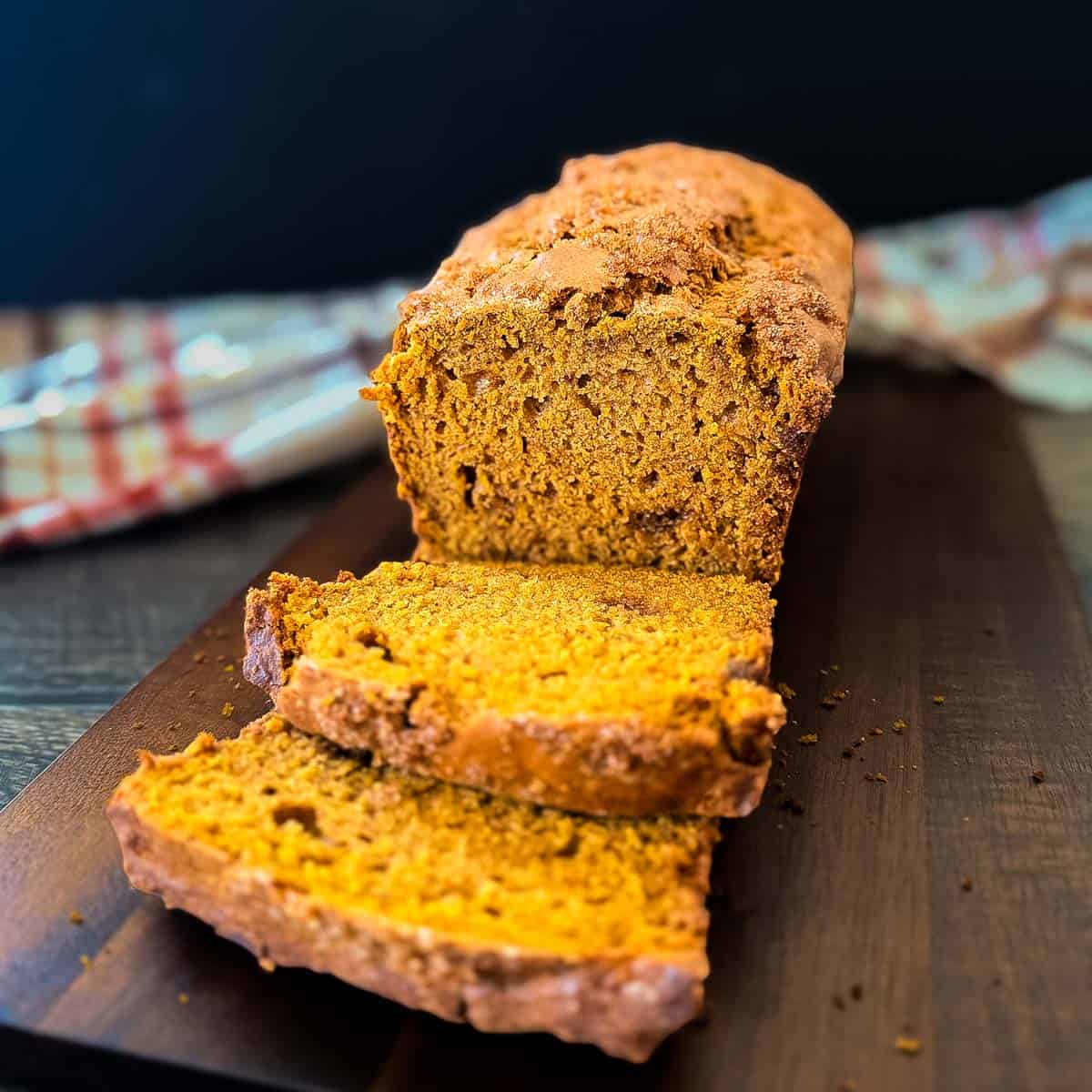 Sliced sourdough discard pumpkin bread on a wooden cutting board, showing the golden crust and soft orange pumpkin crumb.