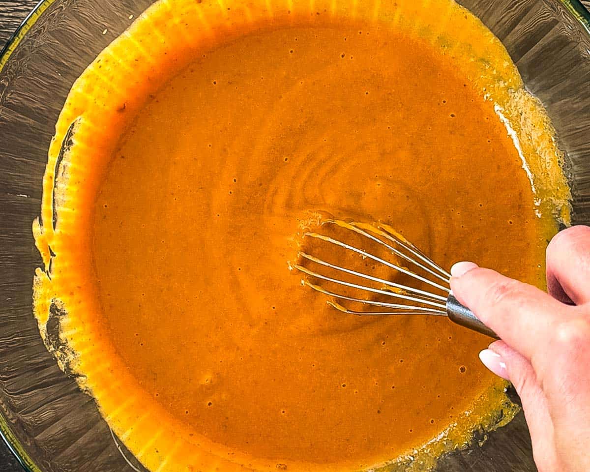Smooth orange pumpkin bread wet ingredients being mixed with a whisk in a glass bowl.