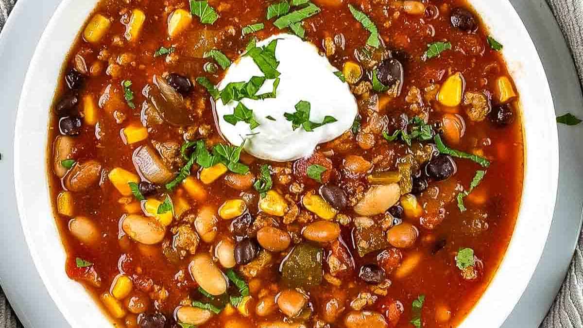 A bowl of ground turkey chili garnished with a dollop of sour cream and fresh cilantro.